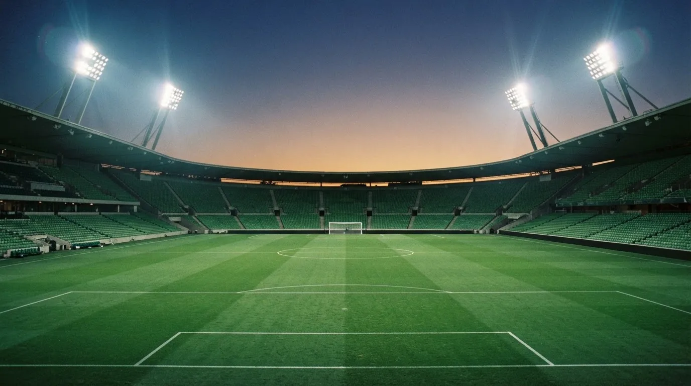 Een leeg voetbalstadion met lichtmasten bij schemering