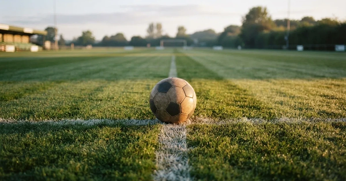 Een voetbal op de middenstip van een grasveld in het ochtendlicht