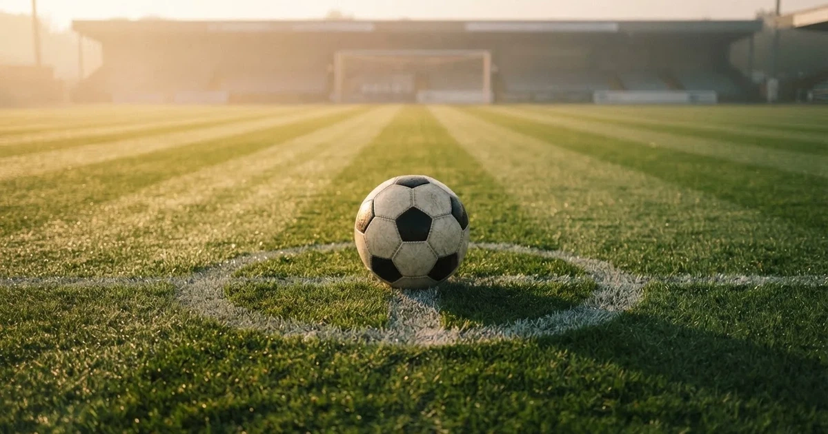 Een voetbal op de middenstip van een grasveld in het ochtendlicht