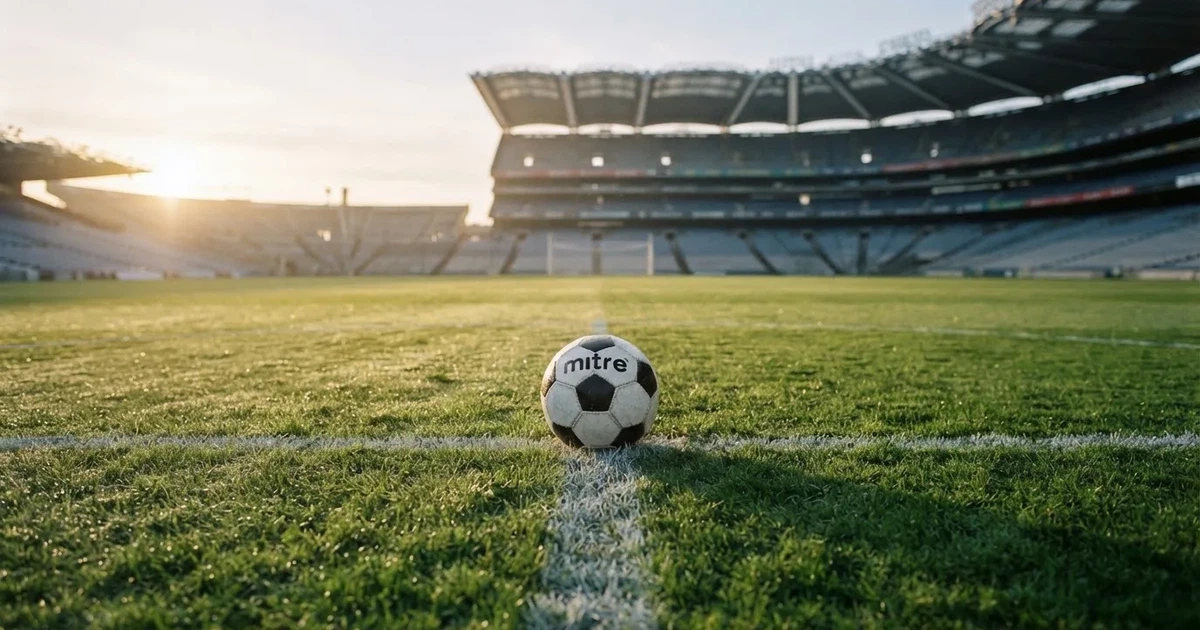 Een voetbal op de middenstip van een grasveld in het ochtendlicht